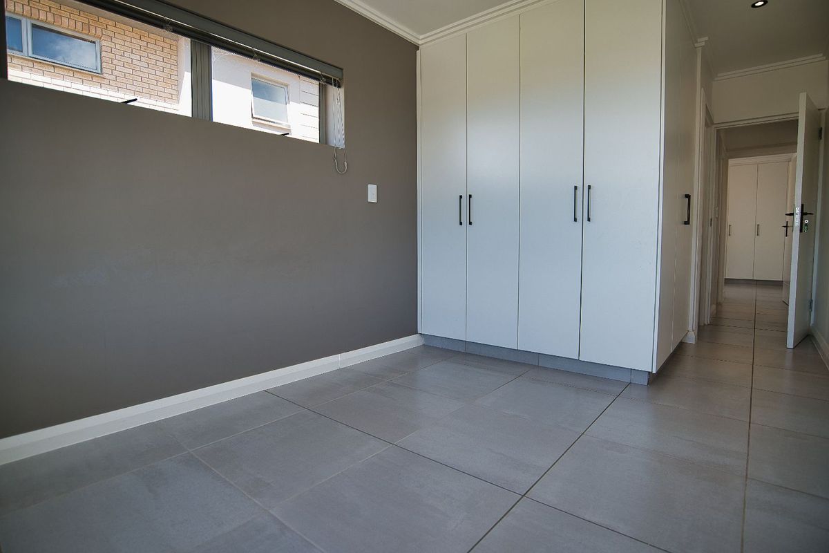 A bright bedroom featuring large format floor tiles, built-in cupboards with modern handles, and a horizontal window providing natural light.