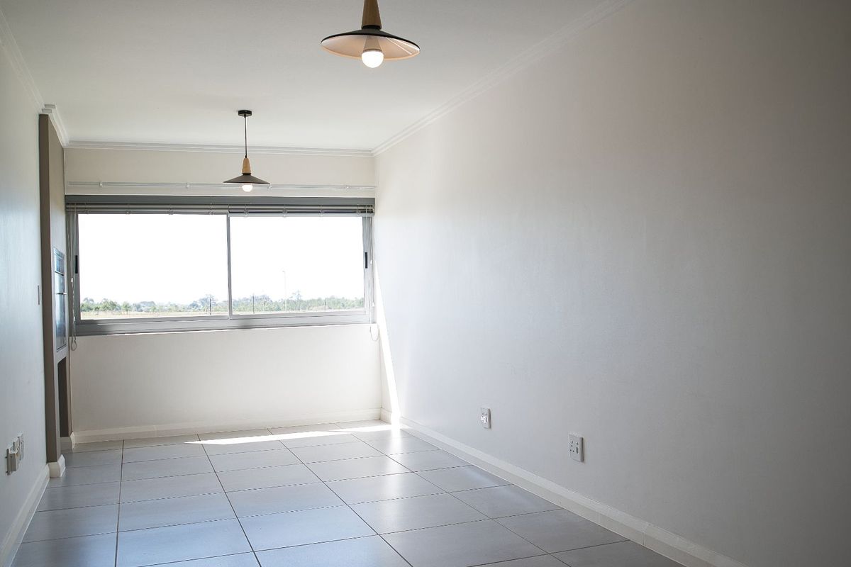 A bright, empty living area featuring neutral tiled flooring, modern pendant lighting, and a large sliding window with views.