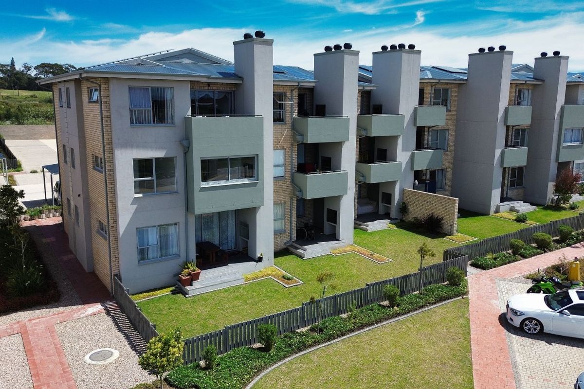 Aerial view of a modern apartment complex featuring multi-story units with private balconies, brick and plaster facades, and landscaped garden areas.