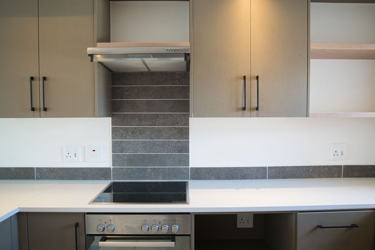 Modern kitchen featuring sleek cabinetry, a built-in electric hob and oven, extractor fan, and a stone-look tiled backsplash with white countertops.