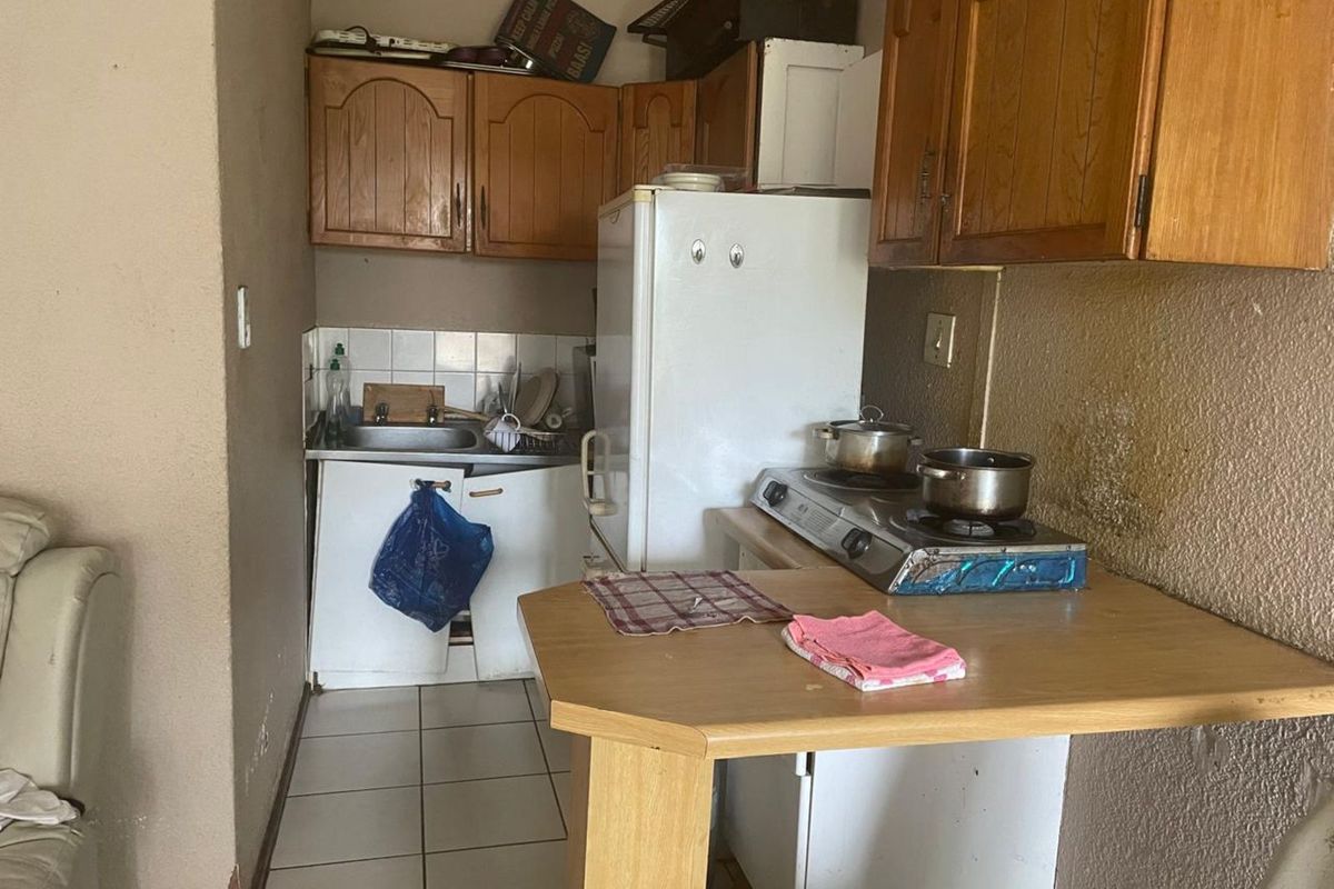 A compact, dated kitchen area featuring wooden cabinetry, a small sink, and a built-in countertop stove, requiring significant renovation and cosmetic updates.
