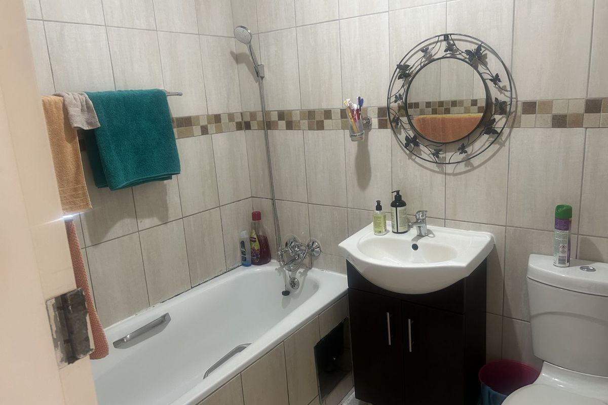 Compact bathroom featuring a bathtub with shower attachment, a vanity basin, and a toilet, finished with neutral wall tiling.
