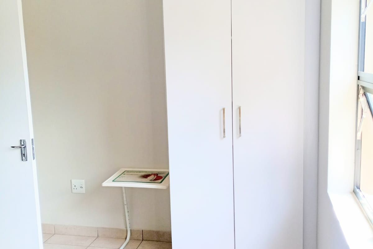 A bedroom featuring tiled flooring and a built-in white wardrobe, providing functional storage space within the apartment.