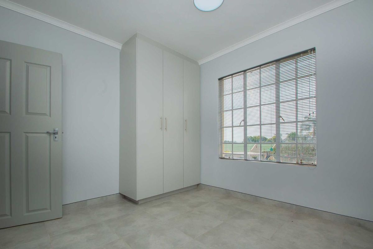 A bright, empty bedroom featuring neutral tiled flooring, built-in cupboards, and a window fitted with horizontal blinds.