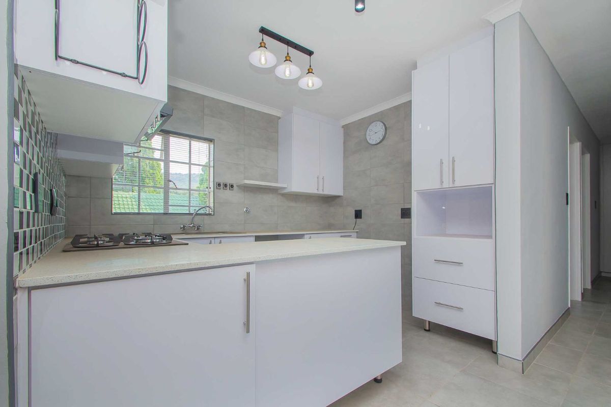 Modern kitchen featuring white cabinetry, stone countertops, a built-in gas hob, and neutral grey wall tiling.