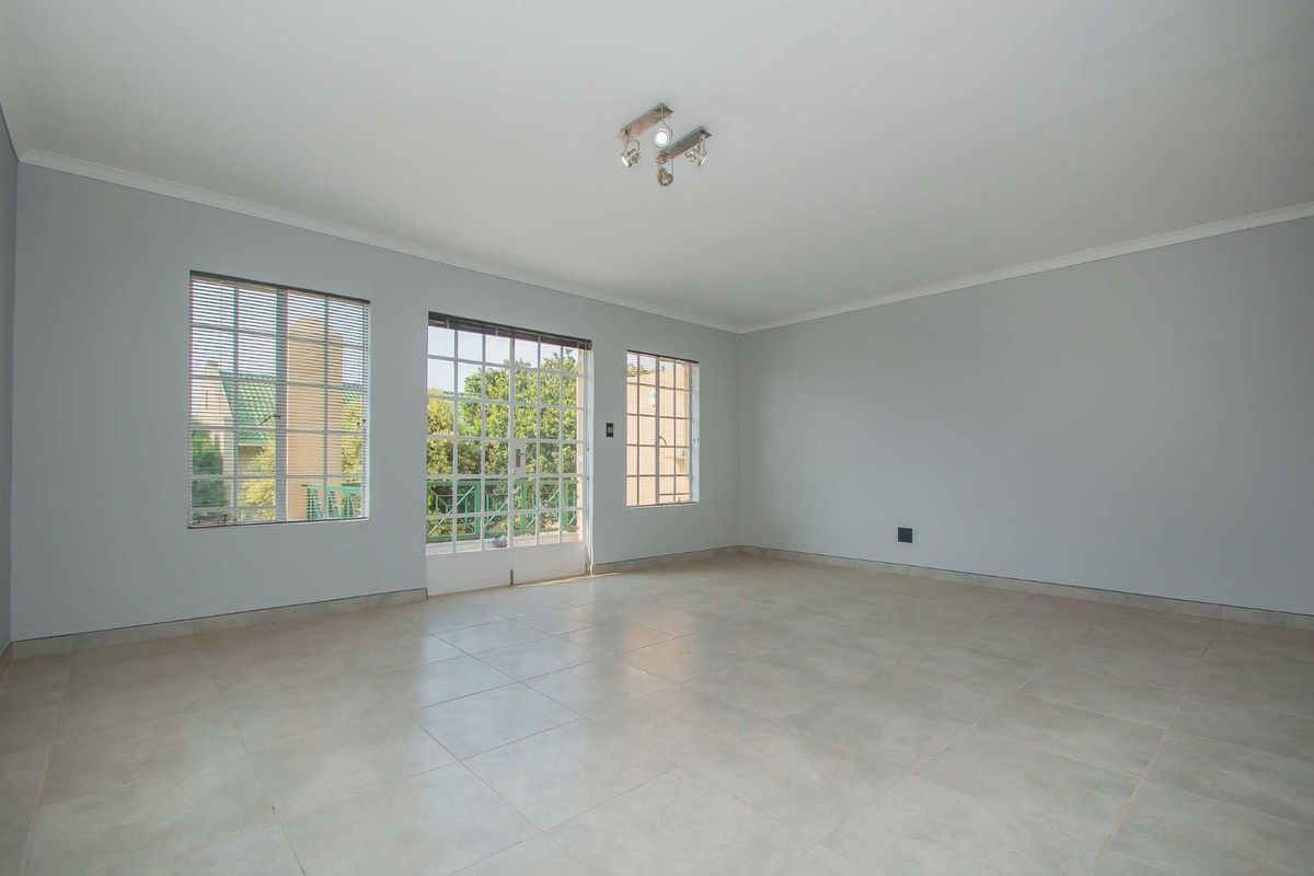 A bright and spacious living area featuring neutral tiled flooring, large windows, and a glass-paneled door providing access to the exterior.