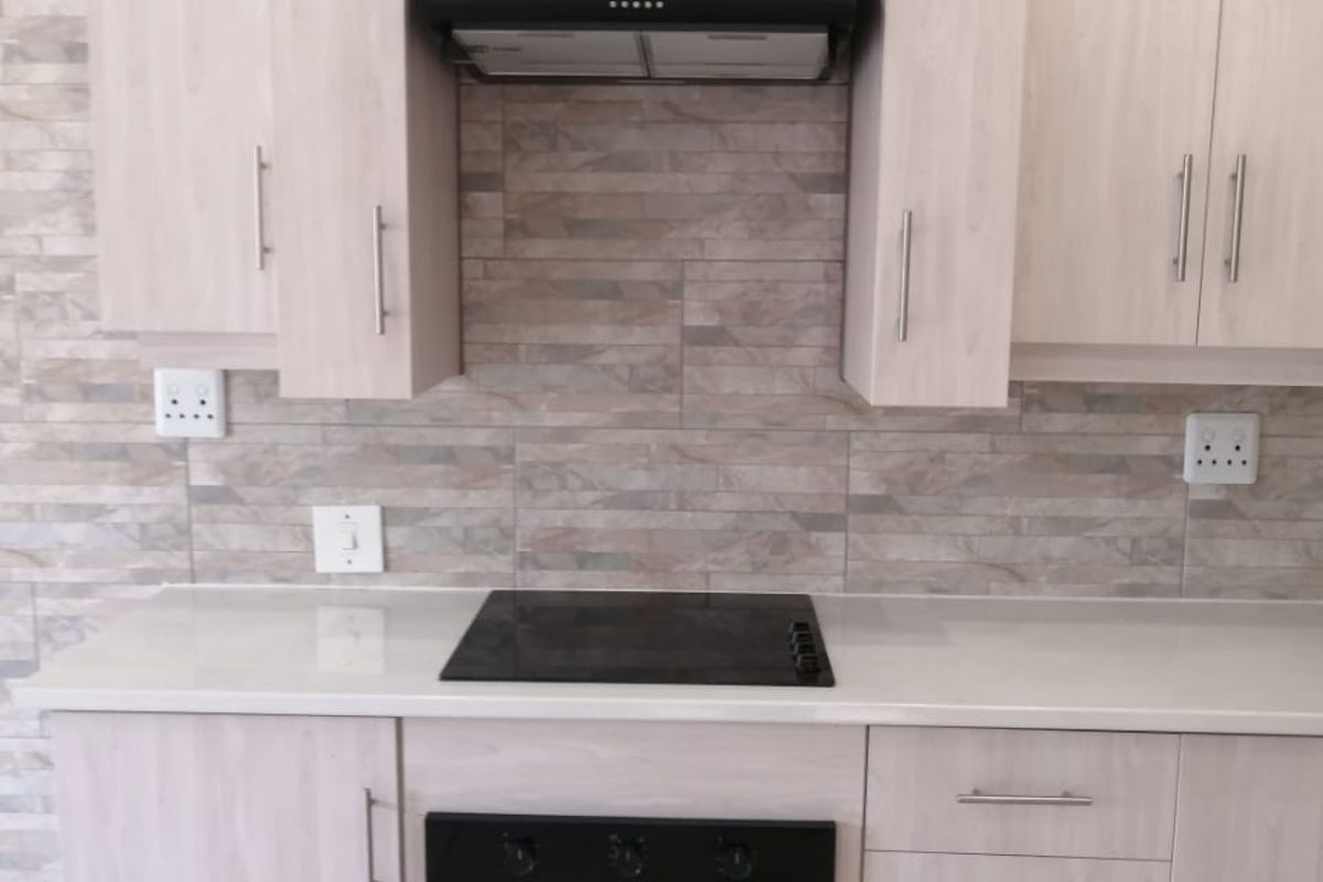 Modern kitchen featuring light wood-grain cabinetry, stone-look tiled backsplash, built-in electric oven, glass cooktop, and a sleek extractor fan.