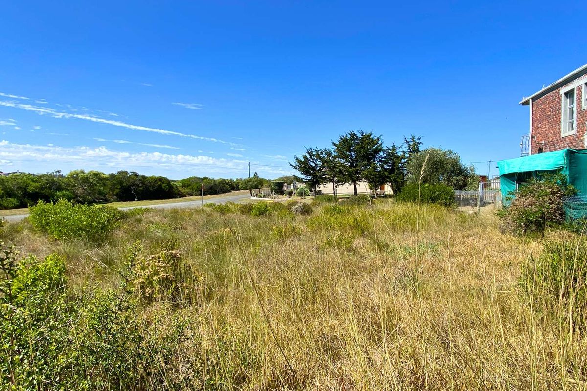 A view of the vacant residential land featuring natural vegetation and surrounding landscape, with a partial view of an adjacent building structure.