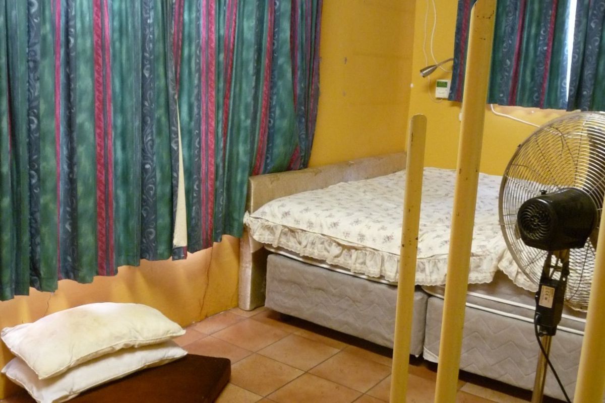 A bedroom featuring tiled flooring, yellow painted walls, and a ceiling fan, providing a functional sleeping space.
