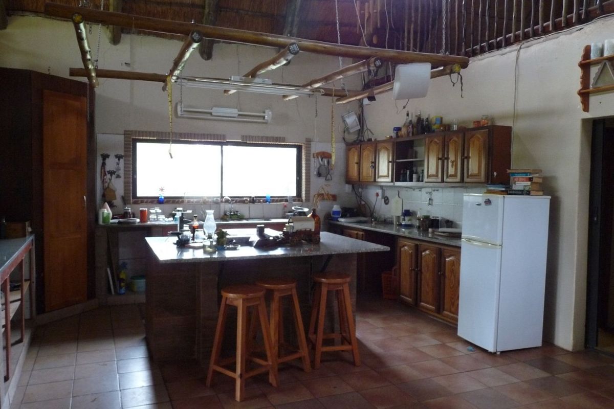 Rustic farm-style kitchen featuring a central island, wooden cabinetry, tiled flooring, and a traditional thatched roof structure.