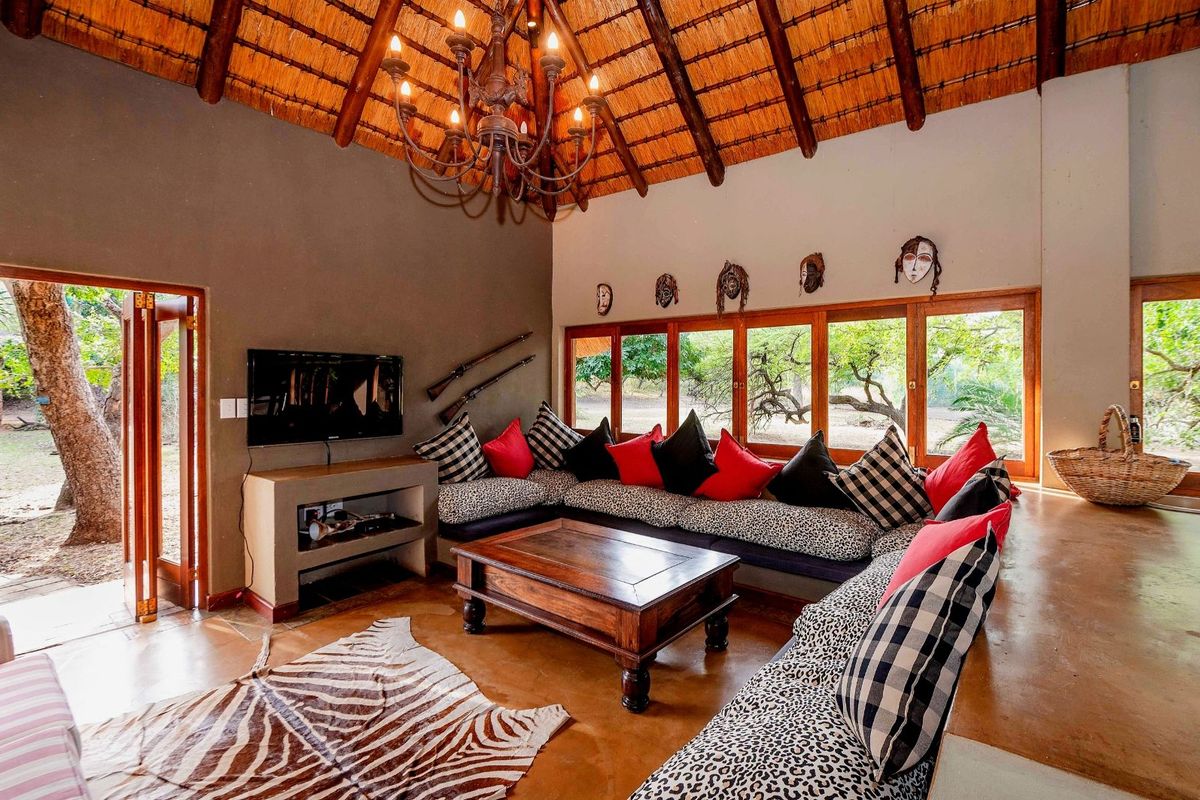 Spacious living room featuring a high vaulted thatched ceiling, exposed timber beams, polished concrete flooring, and large windows providing natural light and garden views.