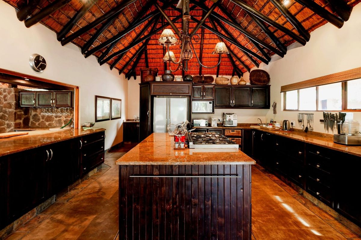 Spacious kitchen featuring dark wood cabinetry, granite countertops, a central island with a built-in gas hob, and a high vaulted thatched ceiling.