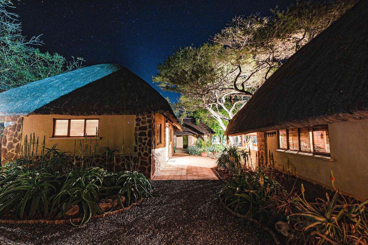 Night view of traditional thatched-roof cottages featuring stone masonry accents, paved walkways, and established garden landscaping under a clear starry sky.
