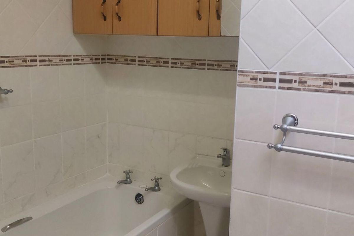 A functional bathroom featuring a bathtub, pedestal basin, and wall-mounted storage cabinetry with neutral tiled walls.