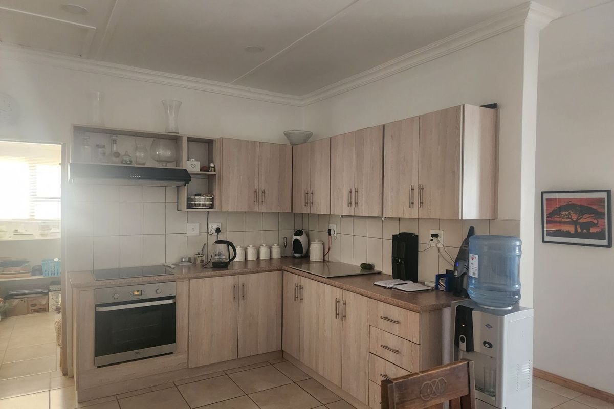 Functional kitchen featuring light wood-grain cabinetry, built-in oven, electric hob, extractor fan, and tiled flooring with an adjacent scullery area.
