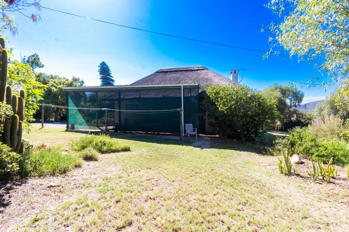 Rear view of a traditional thatched-roof house featuring a covered patio area and established garden surroundings.