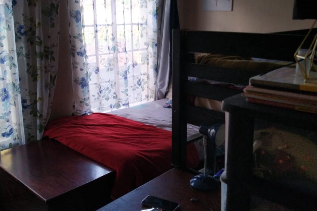 A bedroom featuring tiled flooring and a window fitted with security bars, providing natural light to the space.