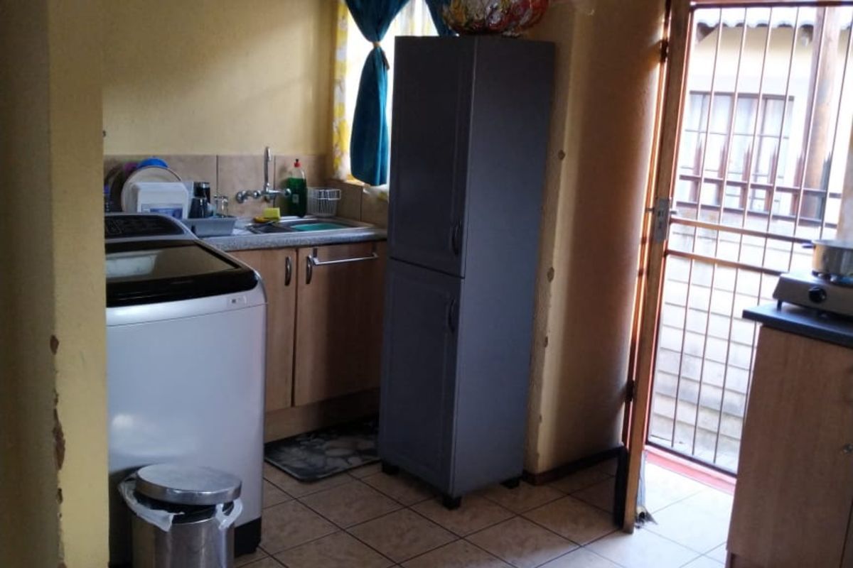 A functional kitchen area featuring tiled flooring, built-in cabinetry, and a sink, with direct access to the exterior via a security gate.