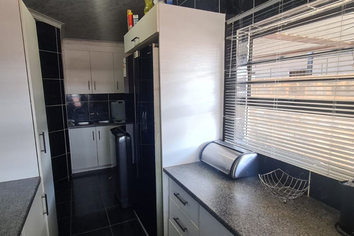 A functional kitchen featuring dark tiled walls, granite-style countertops, and white cabinetry with integrated storage space.