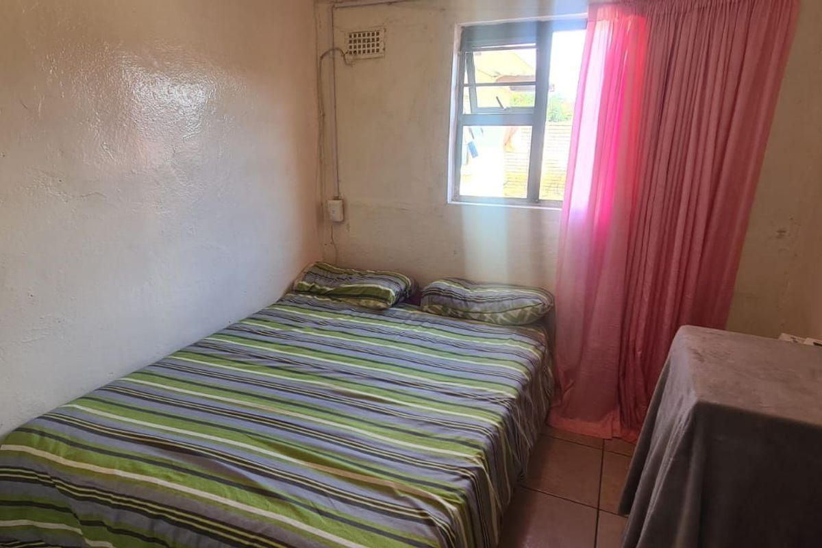 A compact bedroom featuring tiled flooring, a window with natural light, and basic wall finishes.