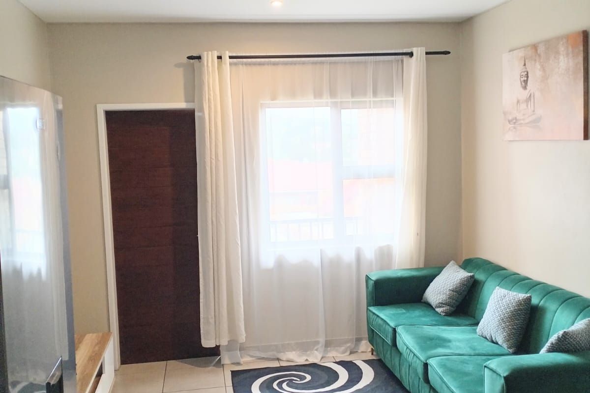 A compact living area featuring tiled flooring, a neutral color palette, and a window with curtain treatments.
