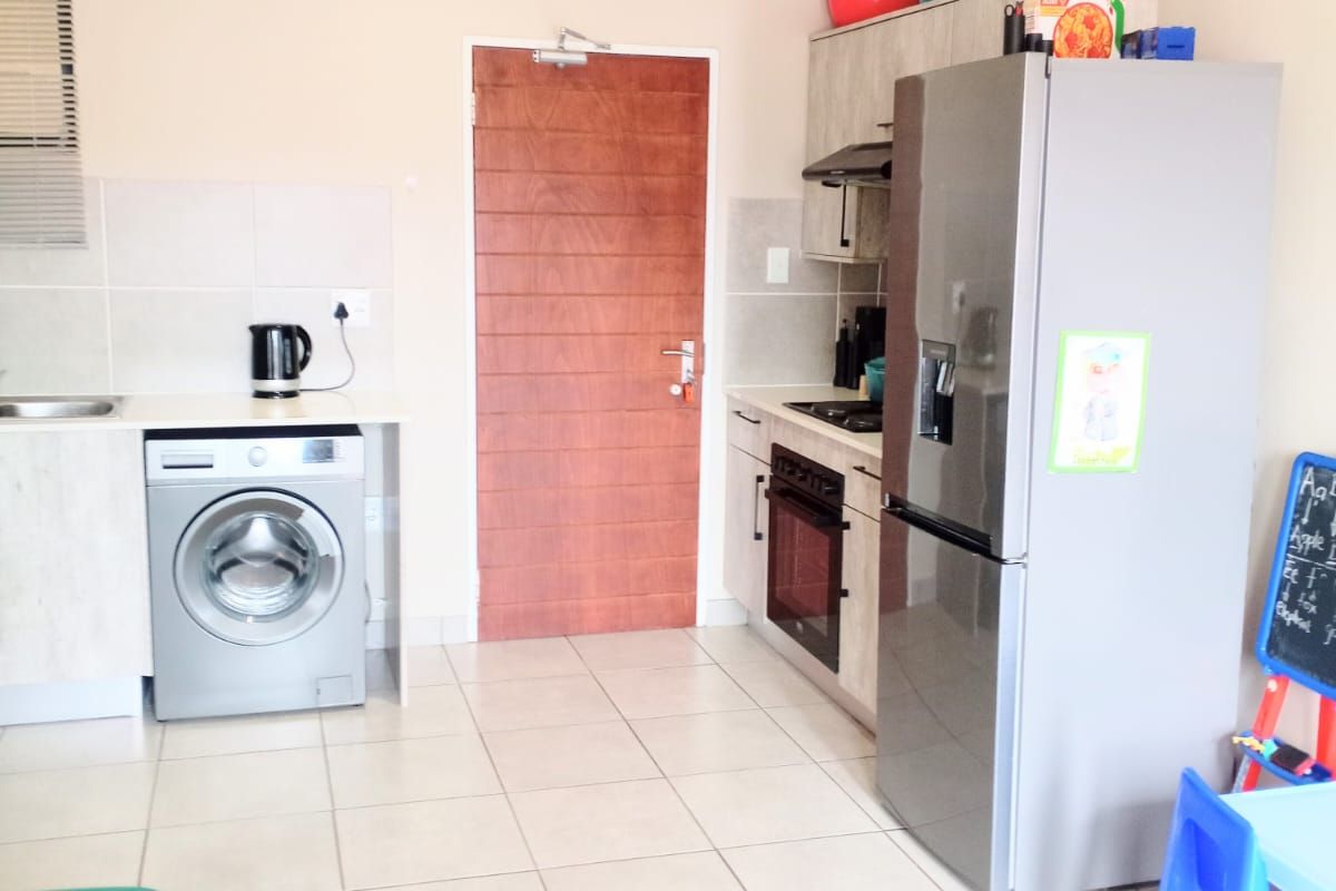 A functional kitchen area featuring built-in cabinetry, a stove, oven, extractor fan, and integrated laundry plumbing, finished with neutral floor tiles.