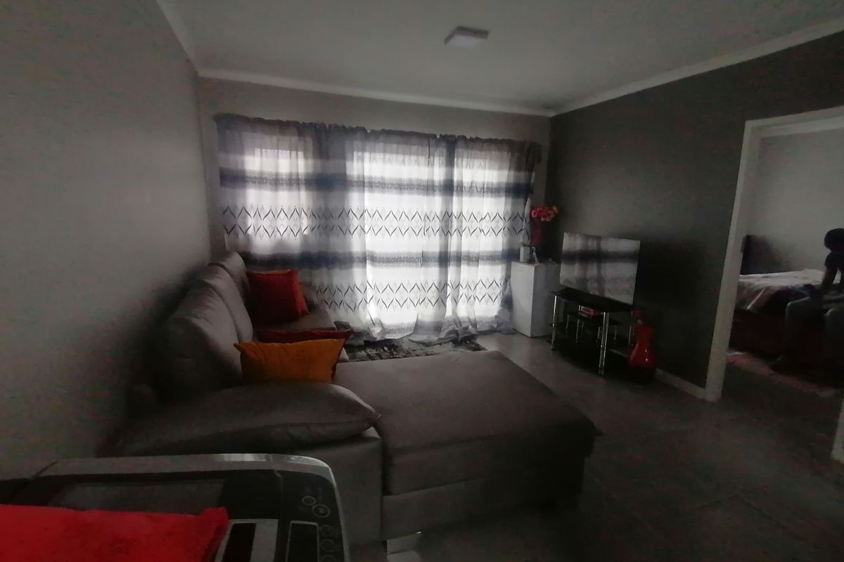 A living room area featuring tiled flooring and a large window with curtains, providing access to an adjacent room.