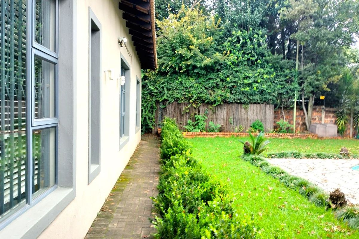 A side view of the property featuring a paved walkway, manicured hedge, and a glimpse of the rear garden and swimming pool area.