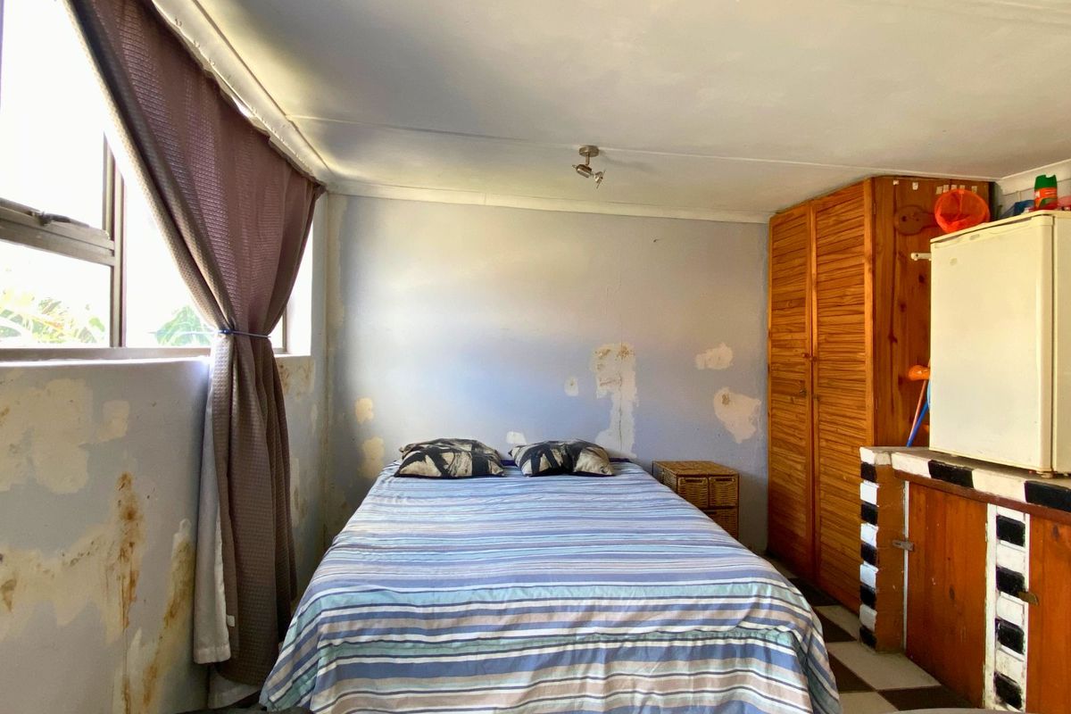 A bedroom featuring built-in wooden cabinetry and a window, currently showing significant wear to the wall finishes requiring maintenance and repair.