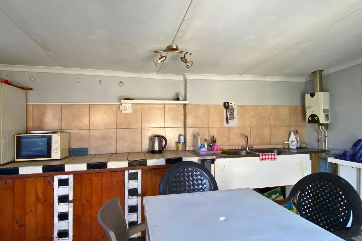 A functional kitchen featuring tiled countertops, wooden cabinetry, a stainless steel sink, and a wall-mounted gas geyser.