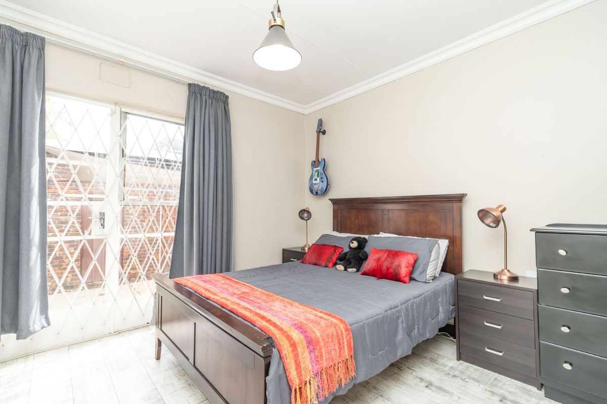 A well-lit bedroom featuring tiled flooring, crown molding, and a sliding glass door with security gate providing access to the exterior.