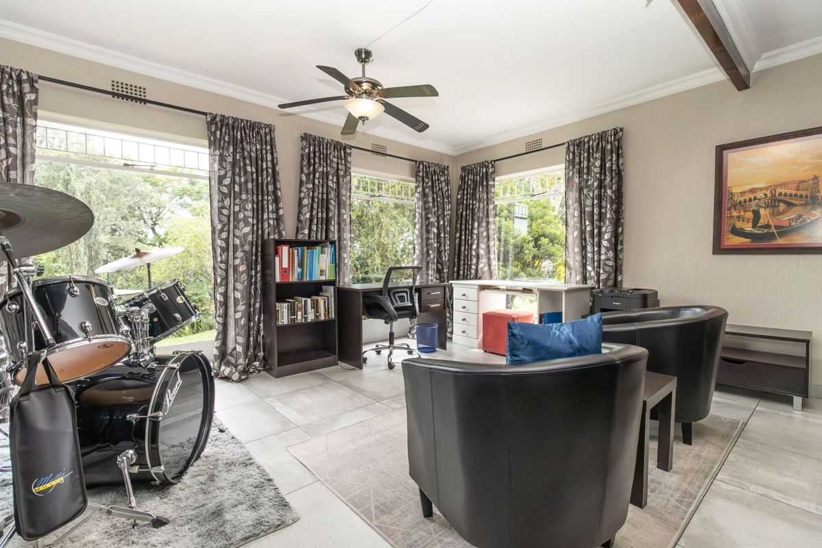 A bright, multi-purpose living space featuring large windows, tiled flooring, and a ceiling fan, currently utilized as a home office and music room.