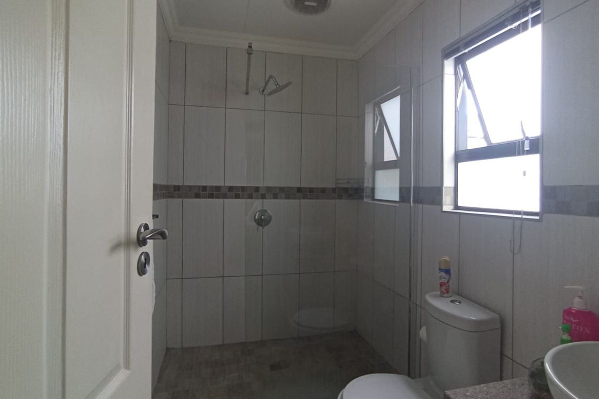 A functional bathroom featuring a walk-in shower with glass partition, a modern toilet, and a vanity basin with tiled walls.