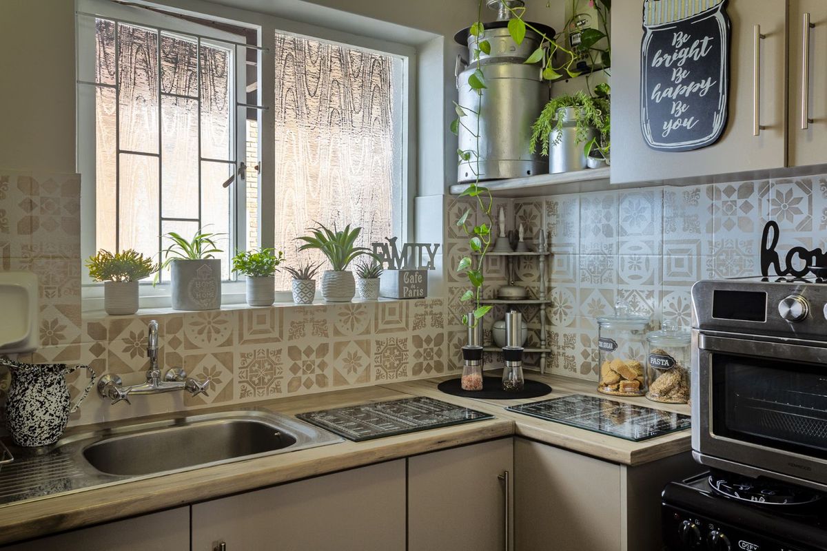 A compact kitchen featuring patterned tile splashbacks, a stainless steel sink, wooden countertops, and built-in cabinetry with an integrated oven.