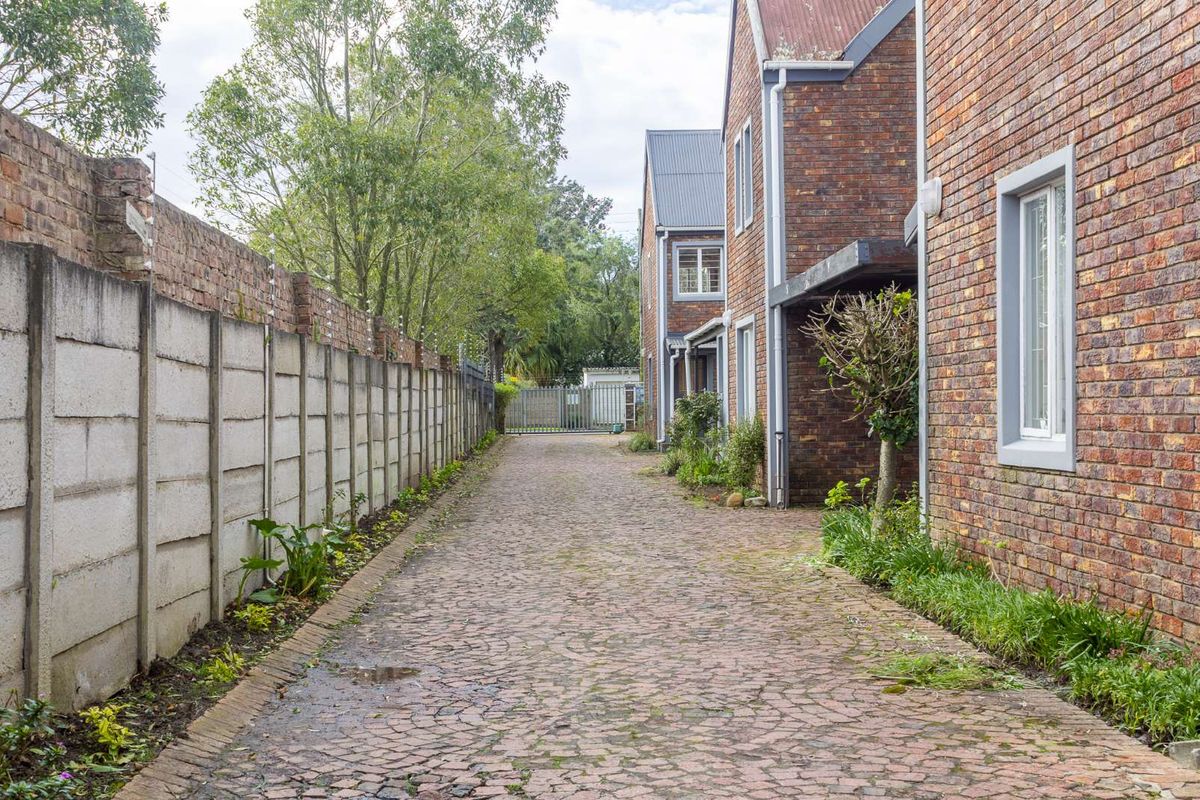 A side access path featuring cobblestone paving, bordered by a brick building facade and a high concrete boundary wall.