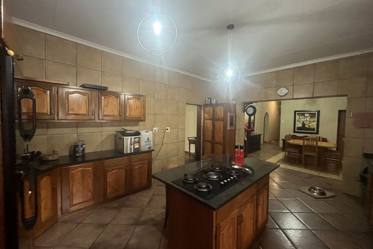 Spacious kitchen featuring wooden cabinetry, a central island with a built-in gas hob, and tiled flooring, opening into an adjacent dining area.