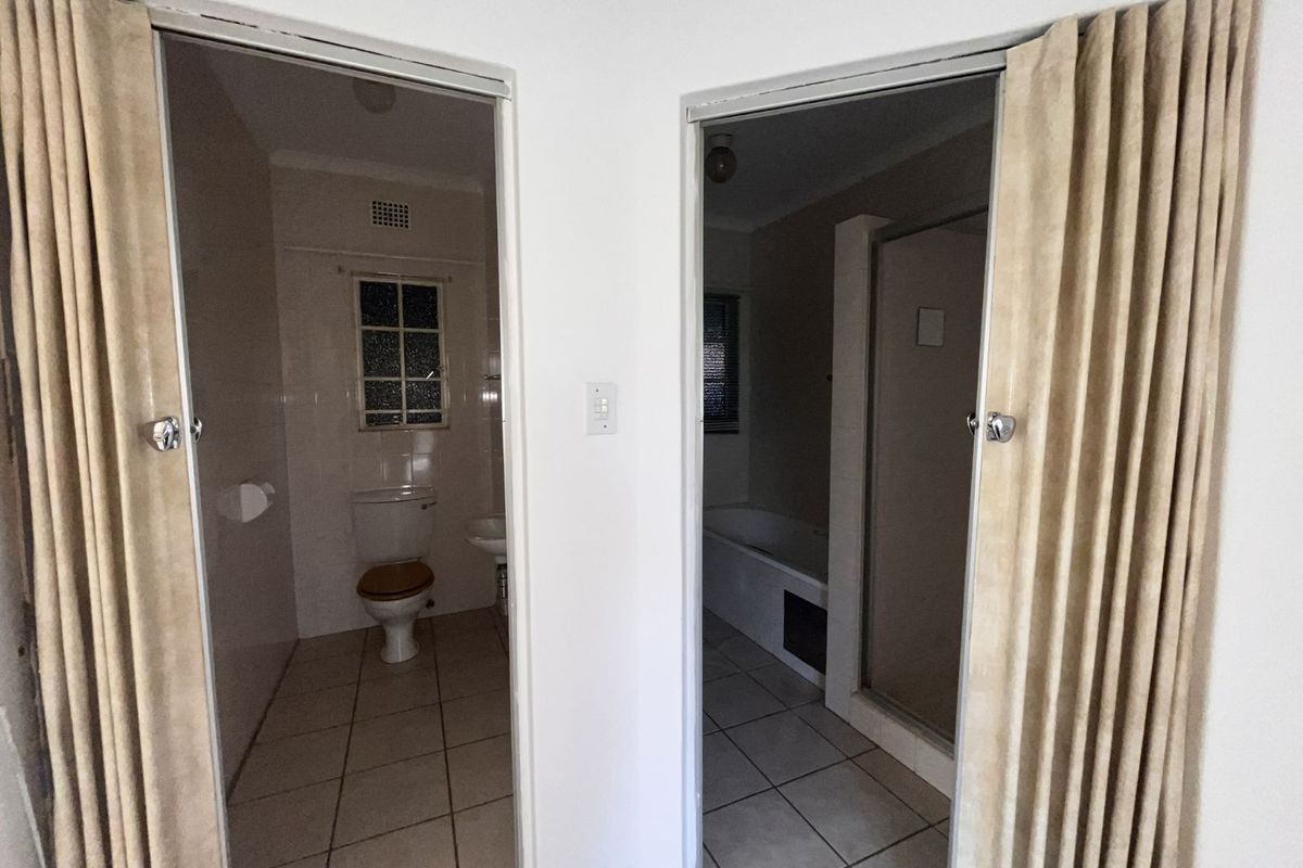 A view into a bathroom featuring a separate toilet area and a combined bath and shower enclosure with tiled flooring.