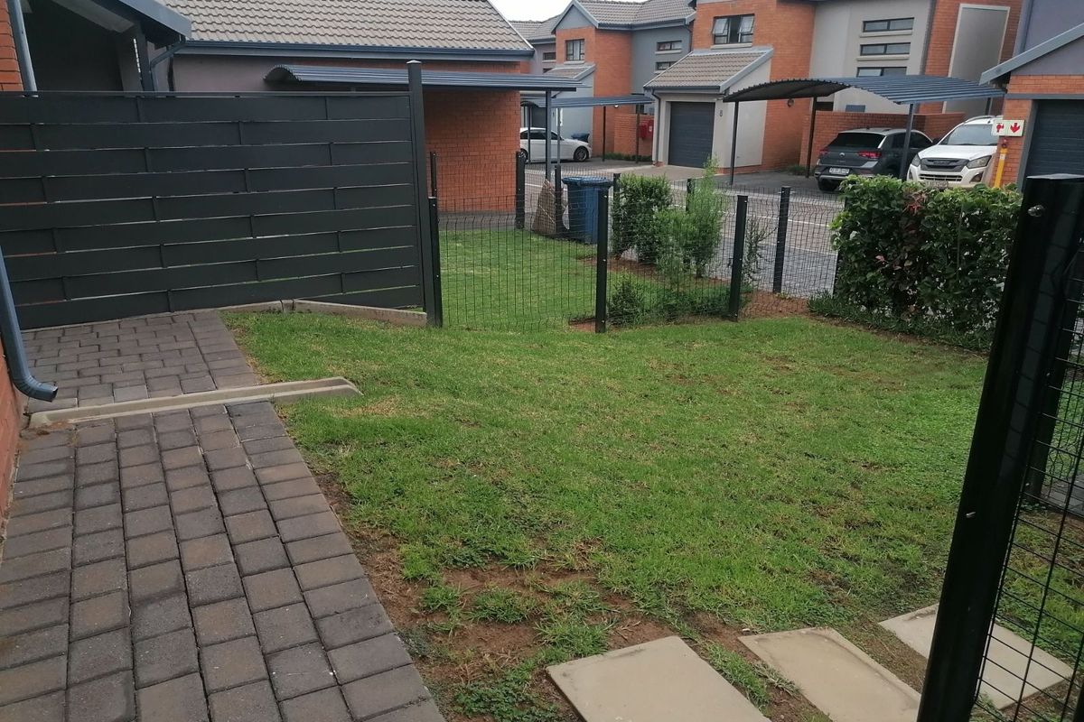 A private rear garden featuring a paved patio area, a small lawn, and perimeter fencing within a residential apartment complex.