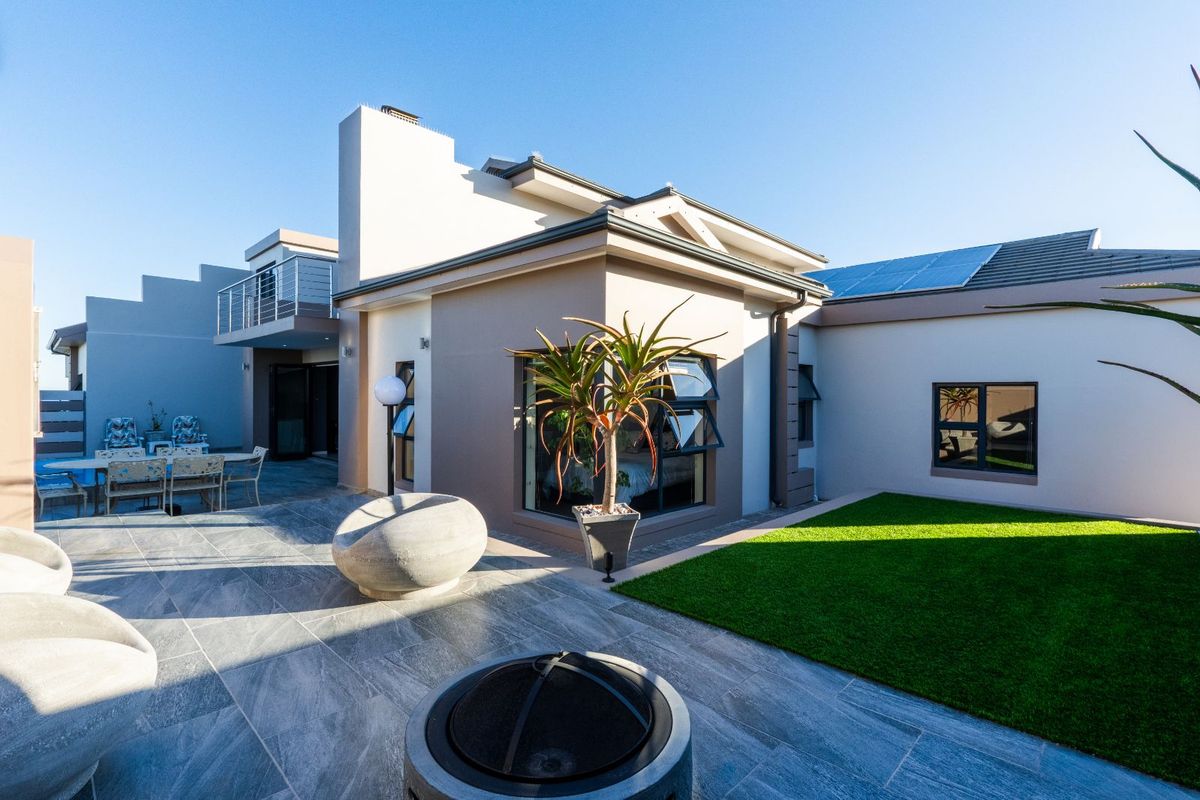 A modern rear exterior view featuring a paved patio area, artificial lawn, and a balcony overlooking the garden space.