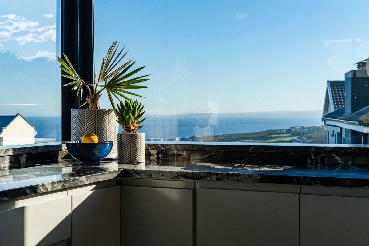 A modern kitchen corner featuring sleek cabinetry and polished stone countertops, perfectly positioned to capture expansive coastal and landscape views.