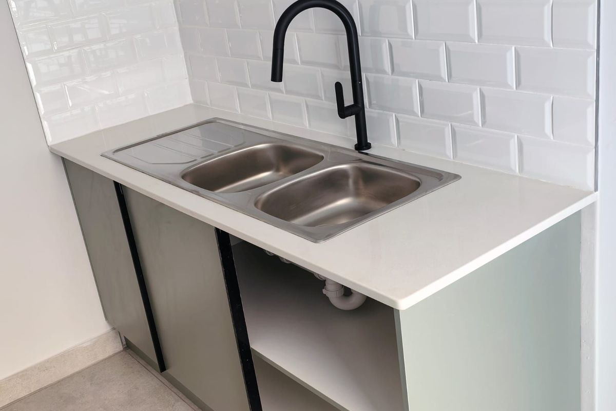 A functional kitchen area featuring a double stainless steel sink, modern matte black faucet, and white subway tile splashback.