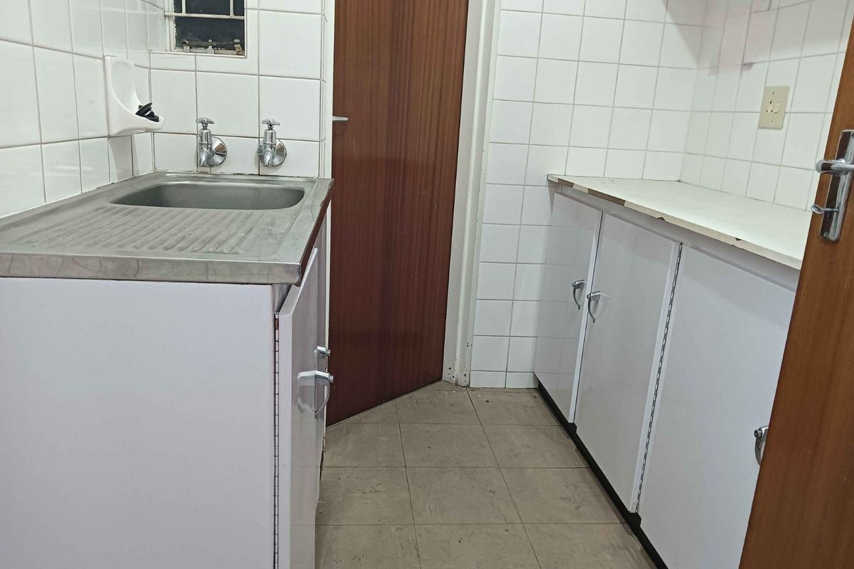 A functional kitchenette or utility area featuring a stainless steel sink, white cabinetry, tiled walls, and tiled flooring.