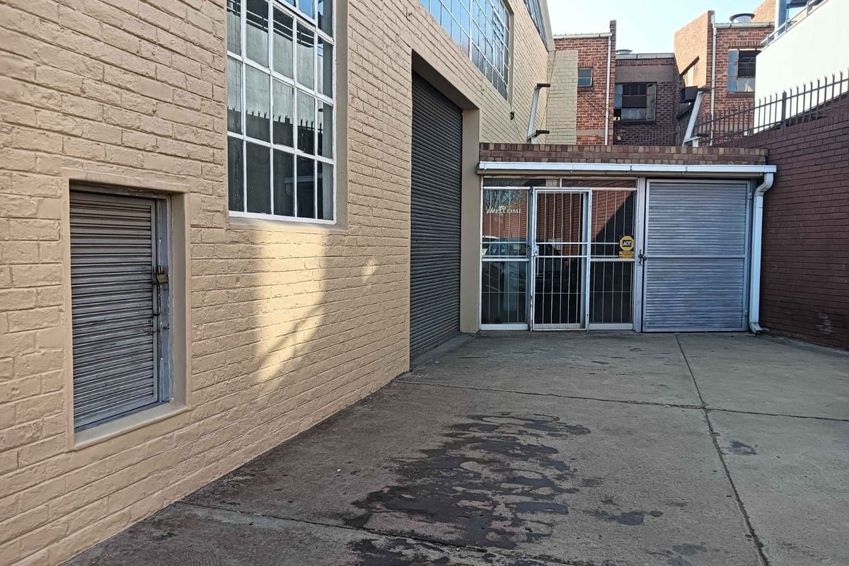Exterior view of the office property featuring a paved courtyard, roller shutter doors, and secure metal entrance gates.