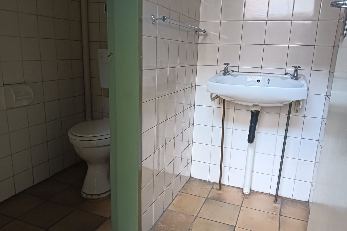 A functional office restroom featuring a wall-mounted basin and a separate toilet cubicle with tiled walls and flooring.