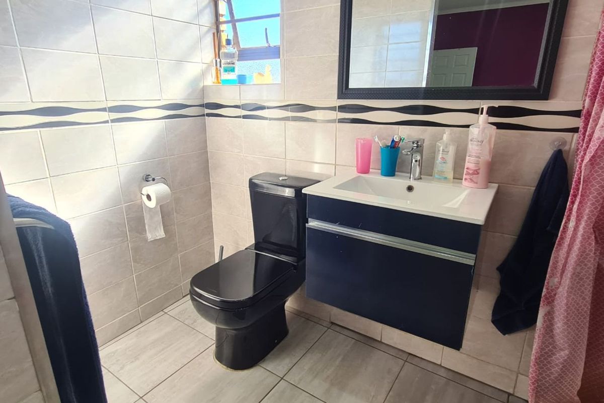 A functional bathroom featuring a wall-mounted vanity with integrated basin, a black toilet, and tiled walls with a decorative border.