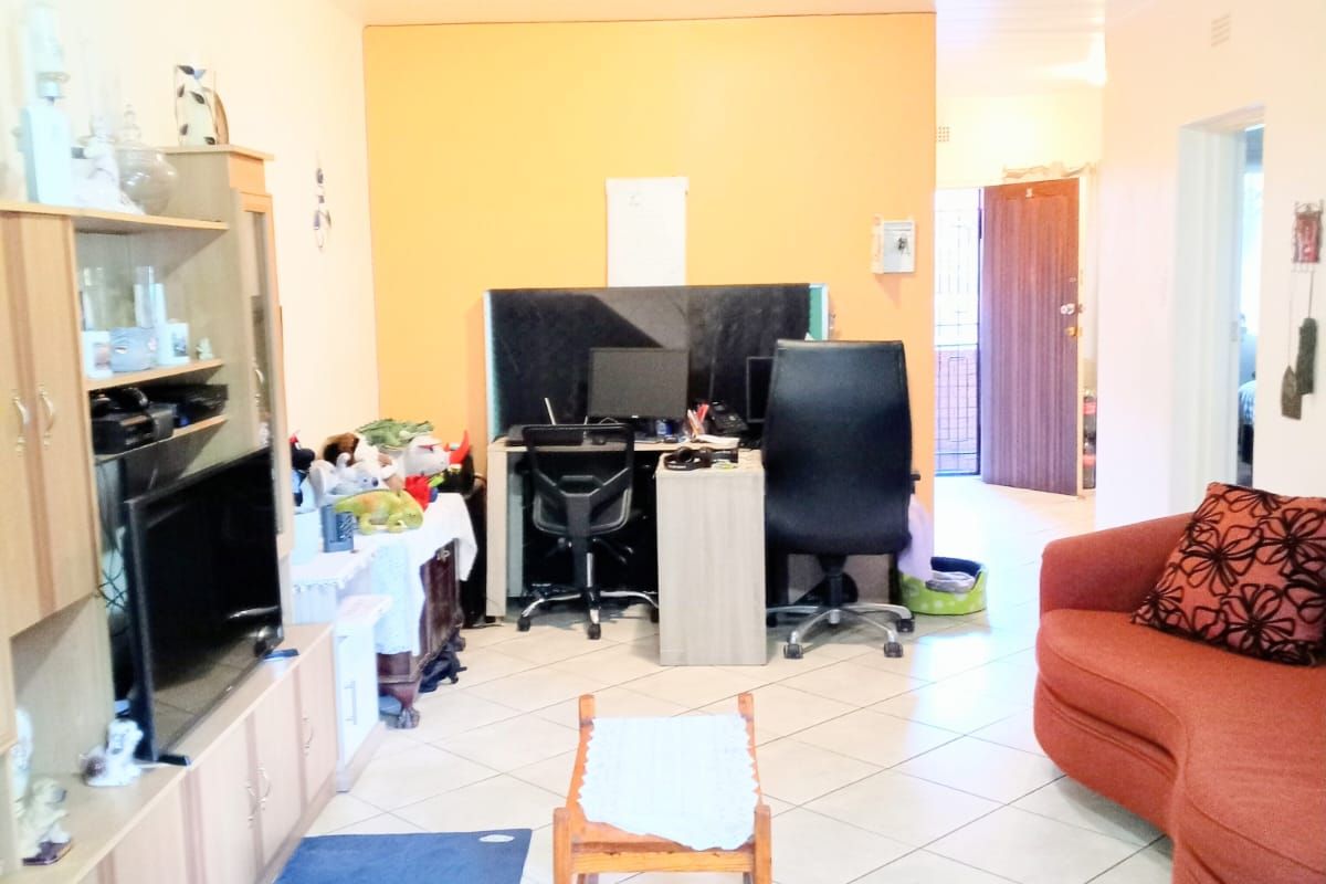 A living room area featuring tiled flooring and an open layout, providing access to the entrance and adjacent rooms.