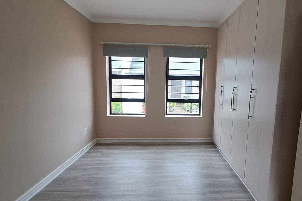 A bright, empty bedroom featuring light-toned wood-look flooring, built-in floor-to-ceiling wardrobes, and dual windows with security bars.