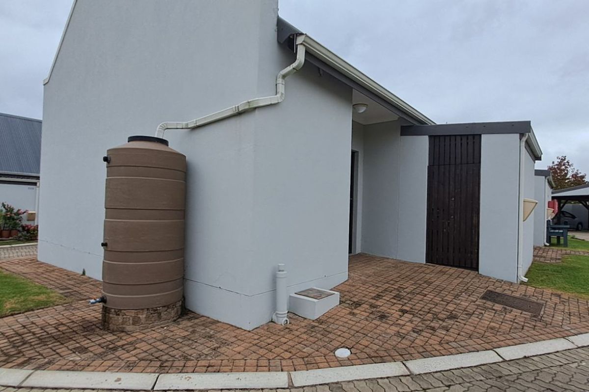 Exterior view of the property side elevation featuring a rainwater harvesting tank, paved driveway, and covered parking area.