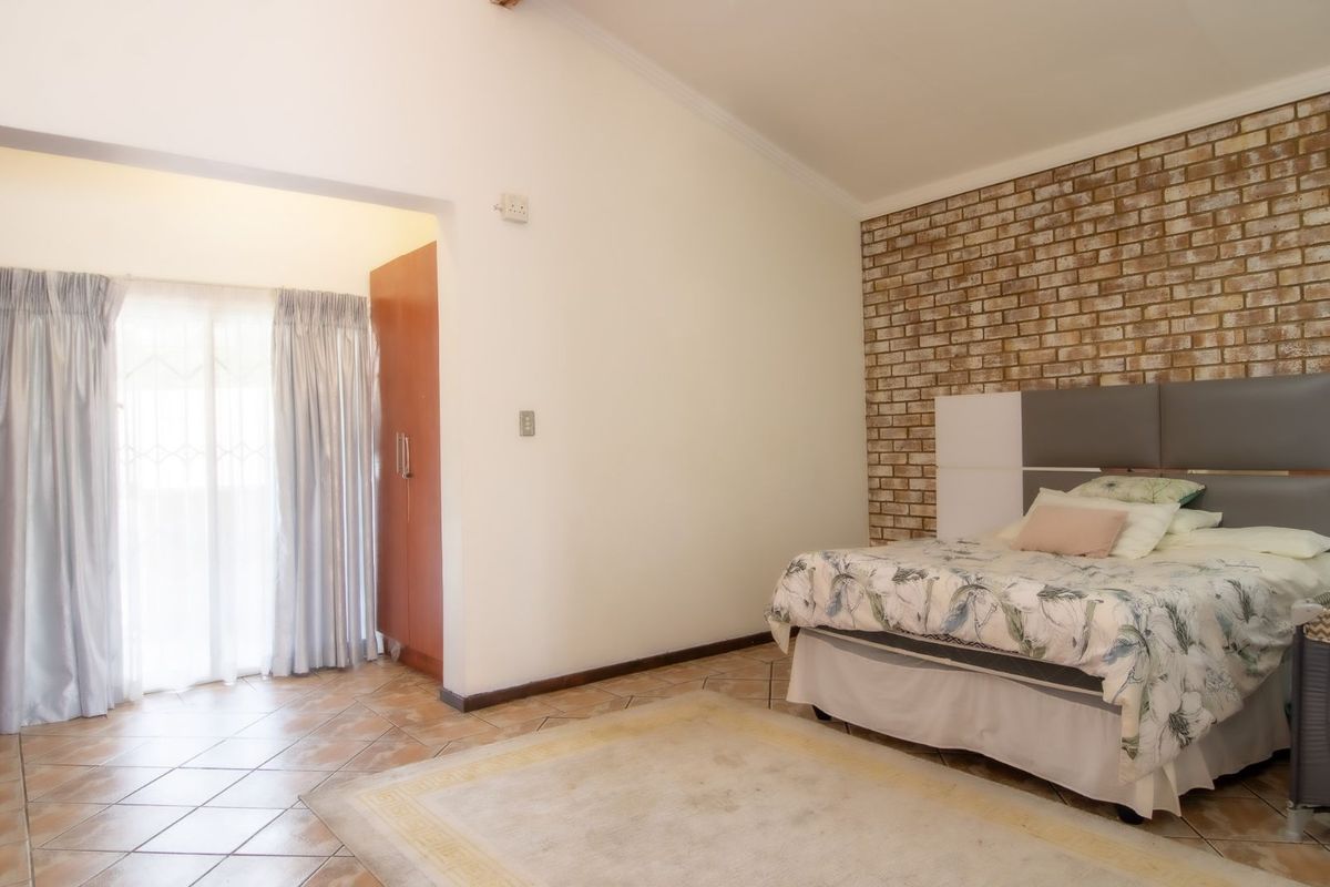 A bedroom featuring a vaulted ceiling, exposed brick feature wall, tiled flooring, and a built-in wardrobe with direct access to an outdoor area.