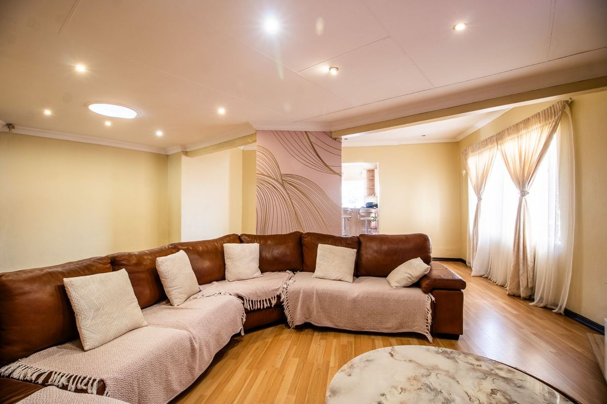 Spacious living area featuring laminate flooring, recessed downlighting, and a decorative feature wall, with an open-plan flow leading to the kitchen area.